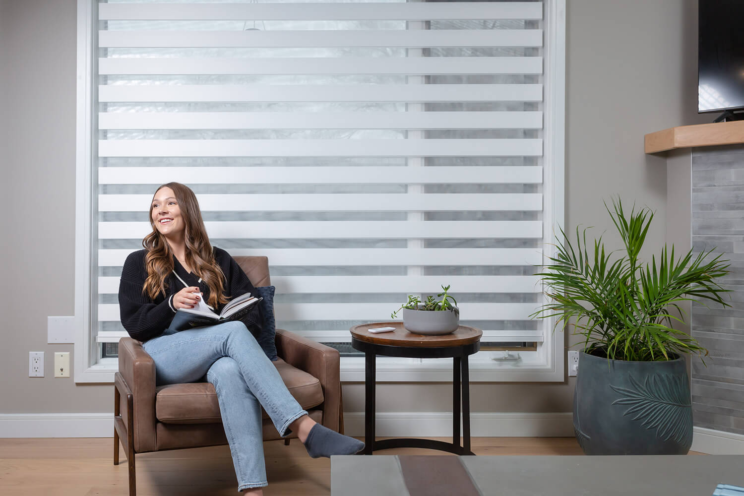 A woman reading beside a large window fitted with zebra shades